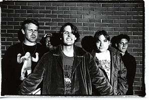 Pavement members standing before a brick wall posing in a black-and-white photo