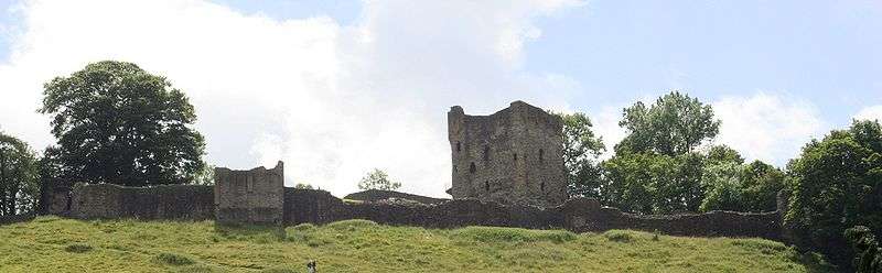 The remains of a low wall in front of a tall stone tower.