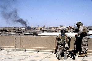 Two Marines on a rooftop observe billowing smoke from an Iraqi city.