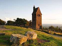 A four storey tower with a steeply pitched roof and chimney on a hillside.