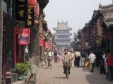 A street lined by traditional houses with red lampions leading to a multi-storied gate.