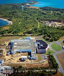 An aerial view of a compound, tree-filled terrain, and blue sea