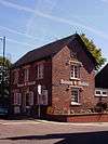 A rectangular, red-brick building, seen from the north-west, at the corner of two streets. Signs on the two visible walls read "Butson & Blofeld".