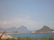 A landscape photograph taken along the shoreline of the Atlantic Ocean on a sunny day. Hills are visible in the background.