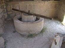 A reconstructed olive press from Volubilis consisting of a circular stone basin with a circular stone inset, atop which a long wooden bar is fixed