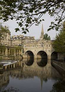 Water in the foreground reflecting an arched bridge of honey coloured stone.