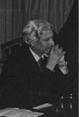 Black and white photo of a man sitting by table.