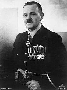 Half-length portrait of a moustachioed man in senior military uniform. He is wearing a group of ten military medals on his breast, with another around his neck and is grasping a sword.