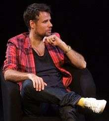 Colour photograph of Richard Bacon sitting on a chair in 2010.