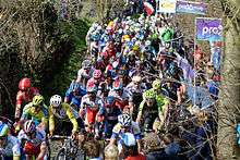 A large group of cyclists on a cobbled road section.