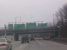 A multilane freeway with a set of four green signs over the road. The left sign reads north Route 440, the second sign reads U.S. Route 9 north Garden State Parkway exit 1/2 mile, the third sign reads Garden State Parkway south no trucks exit 1/4 mile, and the right sign reads U.S. Route 9 south with an arrow pointing to the upper right