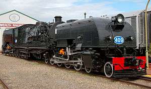 Front oblique view of a black steamtrain with a blue-and-white number 409 on the front and a large shed visible behind.