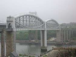 a bridge spanning a river at high level, the bridge deck supported in the centre by curved tubular metal girders