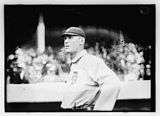 A man in a baseball jersey with a dark cap stands looking up.