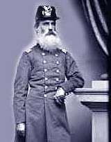 An 1870 black and white photograph of a white male army cavalry officer with a long full white beard age 60 in full military uniform wearing an older style dragoon headwear.