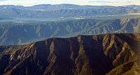 Three mountain ridges cross the foreground with a large lake visible beyond the third ridge and rolling hills beyond the lake