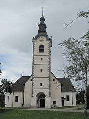 Photo depicts a white stone church with a tall square tower topped by an onion dome.