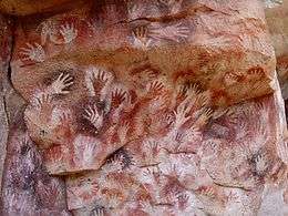 Red and white handprints on a rock face.