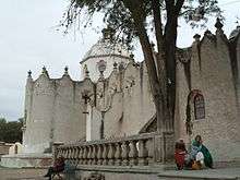 Church with a coppola and massive castle-like walls with small windows.