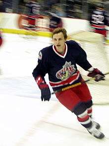 A hockey player in a blue, red and white uniform looks into the distance as he makes a turn while skating.