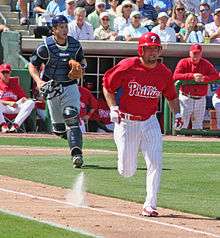 A man wearing a red baseball jersey and cap and white pinstriped baseball pants running on a dirt path