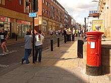 A view looking down Division Street in Sheffield, with a postbox, a Spar shop and pedestrians