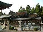 A complex of wooden buildings behind a wooden roofed fence.