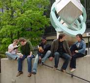 five young people sitting on stone wall in front of modern sculpture and tree