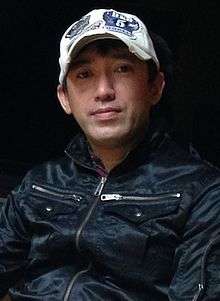 A photograph of a Japanese man wearing a baseball cap.