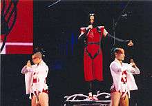 Madonna in a red dress, flanked by her dancers wearing white dress