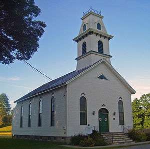 A white church with a rounded steeple and green door