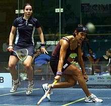 A teammate in a dark blue uniform jumps up while David passes the ball to her.