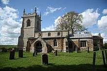 A stone church seen from the south with a belittlemented tower to the left and a smaller chancel to the right