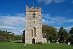 Square stone tower surrounded by trees and grass.