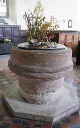 a circular sandstone font standing on an octagonal base, bearing a floral decoration