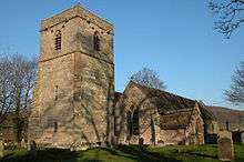 A stone church seen from the southwest, with a tower on the left, and a gabled south aisle and a porch on the right