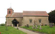 Side view of a building, which has a small tower on the left side: tombstones lie in rows on plots in front.