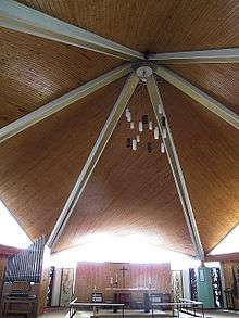 The interior of St Richard's church, Ham, showing the wood-lined ceiling, suspended lights, organ to the left, altar centre with Henry Haig's processional cross behind, flanked by some of his stained glass windows and paintings on the vestry doors