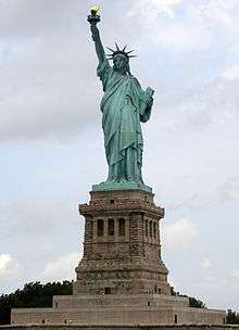 Statue of a robed female figure bearing a torch in her right outstretched arm and a tablet in the other.