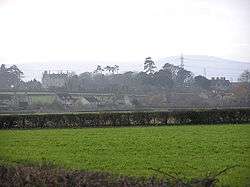 Houses amongst trees seen across fields and hedges.