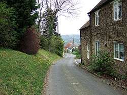 Street scene with a narrow road with houses on the right and trees on the left.