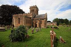 Yellow stone building with square tower set in graveyard.