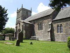 Gray stone building with square tower. Foreground is grass with gravestones.