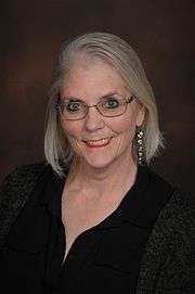 Head shot of Susan smiling with a black background.