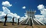 Human sculptures and a hyperbolic shaped modern building with white ribs and glass.