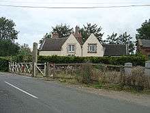 fac-on view of the station building with its two dormer windows.  At some point since conversion to a house it has been whitewashed.  Just visible on the right of the house is the red brick gable of the former goods shed