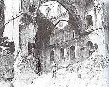 Black & white image of a lone soldier gazing at synagogue interior through a destroyed side wall