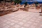 A mosaic made of tiles covers the ground of a small square near a grave site.