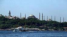 A large building with a square tower, three mosques and ten minarets near water.