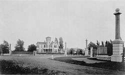 small two story house in middle of monochrome picture, four tall thin plinths surround